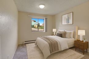 Anchorage apartment for rent - A serene bedroom here at The Continental featuring a queen-sized bed with white bedding and a soft neutral throw, matching bedside tables with lamps, neutral carpet flooring, abstract wall art, and a large window that brings in natural light and neighborhood views.