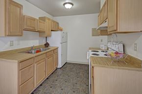 Anchorage apartment for rent - A functional, well-lit kitchen here at The Glen featuring light wood cabinetry, ample countertop space, and a full appliance set including a refrigerator and electric range. Durable flooring and a compact layout create an efficient cooking space that feels clean, bright, and easy to maintain.
