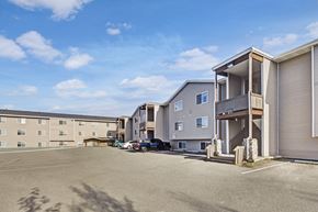 Eagle River apartment for rent - A sunny exterior view here at Timber Ridge featuring multi-story apartment buildings with private balconies, ample parking, and a wide open lot under a bright blue sky for a welcoming community feel.