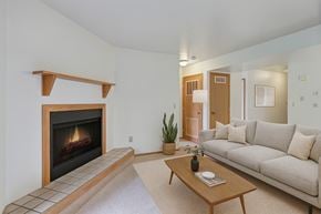 Anchorage apartment for rent - A cozy living room here at Wildwood Estates with a warm corner fireplace, soft neutral carpeting, and a light beige sofa paired with a simple wooden coffee table and tasteful greenery for a clean, inviting feel.