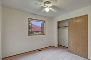 Anchorage apartment for rent - A bright, empty bedroom here at Wildwood Estates with soft carpet, a ceiling fan with overhead light, and a large closet with sliding doors, plus a window that brings in natural light.