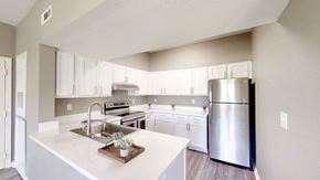 Bentonville apartment for rent - A bright, modern kitchen here at Harbin Pointe featuring crisp white cabinetry, stainless steel appliances, and a spacious peninsula with an undermount sink and quartz-style countertops, complemented by neutral walls, wood-style flooring, and an open layout that connects seamlessly to the living area.