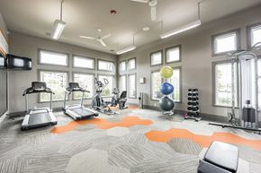 Rogers apartment for rent - A bright modern fitness center here at Palisades at Pleasant Crossing featuring treadmills, an elliptical machine, a stationary bike, a cable weight station, free weights, and stacked exercise balls, with large windows bringing in natural light, ceiling fans overhead, wall-mounted TVs, and patterned flooring with orange accent designs.
