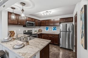 Rogers apartment for rent - A bright, modern kitchen here at Palisades at Pleasant Crossing featuring rich wood cabinetry, stainless steel appliances, light stone countertops with a breakfast bar and undermount sink, pendant and track lighting, a subway tile backsplash, and a clean, open layout designed for everyday cooking and entertaining.
