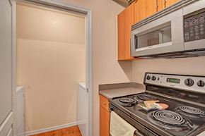 Phoenix apartment for rent - A compact and practical kitchen here at Acclaim featuring light wood cabinetry, laminate countertops, an electric coil cooktop with oven, a built-in microwave, warm wood-style flooring, and an adjacent laundry nook with washer and dryer access tucked just off the kitchen for everyday convenience.
