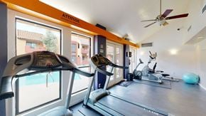 Phoenix apartment for rent - A bright fitness center here at Aspire Pinnacle Park featuring treadmills, elliptical machines, and cardio equipment positioned near large windows overlooking the pool area. Vaulted ceilings with a ceiling fan, motivational wall accents, and durable flooring create an energizing space designed for convenient, comfortable workouts close to home.