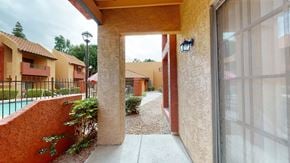 Phoenix apartment for rent - A charming covered patio here at Aspire Pinnacle Park featuring textured stucco walls, a private entryway, and a sliding glass door that brings in natural light. The walkway overlooks landscaped grounds and a sparkling pool area, offering a cozy outdoor space to relax while enjoying the community’s inviting courtyard setting.