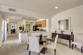 Anthem apartment for rent - A spacious open dining and kitchen area here at Bela Rosa featuring plush carpeting, a round dining table with upholstered chairs, and a raised breakfast bar overlooking the kitchen. Light wood cabinetry, stainless steel appliances, and recessed lighting complement the airy layout, while a sliding glass door brings in natural light and extends the living space outdoors.