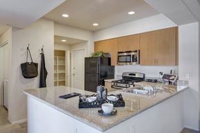 Anthem apartment for rent - A bright open kitchen here at Bela Rosa featuring light wood cabinetry, granite-style countertops, and a spacious breakfast bar with an undermount sink. Stainless steel appliances and recessed lighting enhance the modern layout, while an adjacent hallway with built-in shelving adds convenient storage and seamless flow into the living areas.