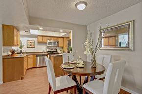 Scottsdale apartment for rent - A welcoming dining area here at Desert Horizon featuring wood-style flooring, a round dining table with seating for four, and decorative wall accents. The space opens to a kitchen with warm wood cabinetry, granite-style countertops, and stainless-steel appliances. Recessed lighting and a large mirror enhance the bright, open layout.