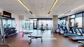 Phoenix apartment for rent - A contemporary fitness center here at JOY on 4th featuring floor-to-ceiling windows with expansive city views, rows of treadmills and cardio machines, free weights with a full dumbbell rack, adjustable benches, and dedicated space for strength training. Sleek lighting, rubber flooring, and mirrored walls create an energizing, modern workout environment.