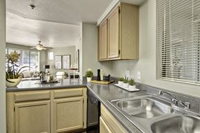 Phoenix apartment for rent - A functional kitchen here at Mirador featuring light wood cabinetry, gray countertops, and a double-basin stainless sink beneath a window with white blinds. The open layout flows into the adjacent living area, while decorative accents, small plants, and ample counter space create a bright and practical setting for everyday cooking and entertaining.