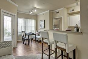 Phoenix apartment for rent - A stylish dining and kitchen area here at Mozaic at Steele Park featuring wood-style flooring, a breakfast bar with seating, and track lighting overhead. Large windows with vertical blinds and a glass door bring in natural light, while the open layout connects the dining space seamlessly to the kitchen for easy entertaining.