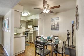 Phoenix apartment for rent - A welcoming dining area here at Paradise Falls showcasing a round dining table set for four beneath a ceiling fan, with wood-style flooring and neutral walls, flowing into a compact kitchen with light cabinetry, ample counter space, and coordinating décor that creates a functional and inviting space for everyday meals and entertaining.