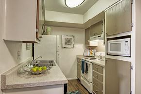 Phoenix apartment for rent - A compact kitchen here at Paradise Falls featuring light cabinetry, generous countertop space, and a functional layout with a sink, range, built-in microwave, and refrigerator, complemented by wood-style flooring and neutral finishes that create an efficient, well-organized space ideal for everyday cooking and meal preparation.