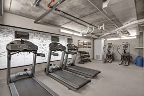 Phoenix apartment for rent - A modern fitness center here at Proxy 333 featuring multiple treadmills with mounted screens, elliptical machines, and a free weight rack set on durable flooring, with an industrial-style exposed concrete ceiling, bright overhead lighting, and clean neutral walls creating a functional and energizing workout space.