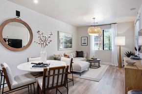 Mesa apartment for rent - A bright and inviting open living and dining area here at Reflect at Dobson Ranch featuring a round dining table with upholstered chairs, a cozy sectional sofa with neutral and warm accent pillows, light wood-style flooring, layered rugs, soft window treatments, modern wall art, and natural light that creates a comfortable and welcoming atmosphere.