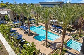 Mesa apartment for rent - A resort-style pool here at Reflect at Dobson Ranch featuring a sparkling rectangular swimming pool surrounded by tall palm trees, spacious concrete decking, rows of lounge chairs with navy umbrellas, and landscaped greenery, creating a relaxed outdoor retreat with shaded seating areas and a clean, modern community atmosphere.
