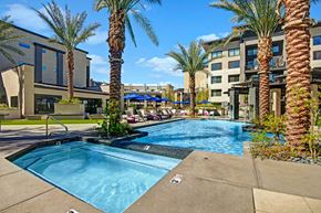 Phoenix apartment for rent - A resort-style outdoor pool here at Roosevelt Row featuring a clear blue swimming pool with an adjacent spa, palm trees throughout the courtyard, modern lounge chairs with umbrellas, landscaped planters, and surrounding contemporary apartment buildings that create a relaxing, upscale community setting.