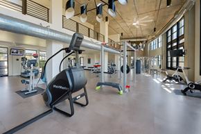 Phoenix apartment for rent - A spacious fitness center here at Roosevelt Row showcasing an open-concept gym with high ceilings, exposed ductwork, large windows for natural light, and a variety of cardio machines, strength equipment, and free weights arranged across polished flooring, creating a modern and motivating workout environment.
