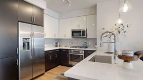 Phoenix apartment for rent - A modern kitchen here at Roosevelt Row featuring a sleek white waterfall island with an undermount sink and tall spring faucet, pendant lighting overhead, contrasting white upper and dark lower cabinets, stainless steel appliances, a geometric tile backsplash, and warm wood-style flooring that creates a clean, contemporary, and functional cooking space.