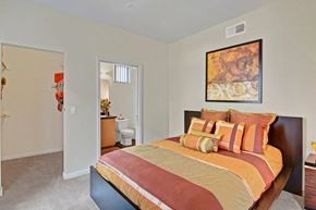 Peoria apartment for rent - A bedroom with a large red bed and a painting on the wall at Visions Apartments.