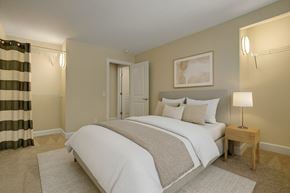 Calgary apartment for rent - A cozy bedroom here at 3600 Brentwood with soft neutral carpeting, a comfortable bed with crisp white bedding, and warm accent lighting, featuring open closet storage and a clean, modern feel.