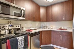 Calgary apartment for rent - A stylish kitchen here at 3600 Brentwood with rich wood cabinets, speckled granite-style countertops, and stainless steel appliances including a microwave, dishwasher, and stove for a modern, functional space.
