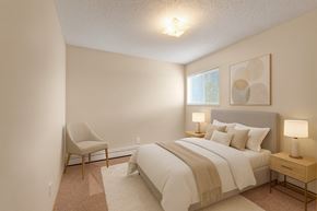 Camrose apartment for rent - A cozy bedroom here at Aspen Terrace with beige carpet, soft neutral walls, and a gray upholstered bed dressed in crisp white bedding and a warm tan throw. A window with blinds brings in natural light, and matching nightstands with modern lamps create a calm, inviting feel.