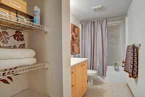 Camrose apartment for rent - A functional bathroom here at Aspen Terrace with a bathtub-shower combo, a light wood vanity with a white countertop, and a clean tile floor. A built-in shelving area with wire racks adds convenient storage, giving the space a practical, welcoming feel.