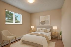 Wetaskiwin apartment for rent - A cozy bedroom here at Birch Terrace with plush beige carpet, a soft neutral color palette, and a window with blinds for natural light. A comfortable bed with matching nightstands, warm lamps, and simple wall art creates a calm, inviting feel.