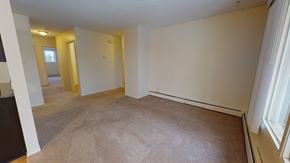 Edmonton apartment for rent - A spacious living area here at Broadmoor with soft carpet flooring, neutral walls, and a wide window that brings in natural light. A long baseboard heater runs along the wall, and the open layout connects smoothly to the hallway for an easy, comfortable flow.