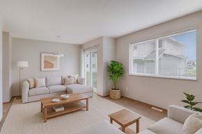 Grande Prairie apartment for rent - A bright living room here at Carrington Place with a light beige sectional sofa, wooden coffee table, and soft neutral décor, featuring large windows, a cozy floor lamp, and a glass door that brings in natural light.