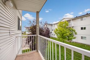 Grande Prairie apartment for rent - A private outdoor balcony here at Carrington Place with sturdy white railing and an open view of the community grounds, featuring lush green landscaping, mature trees, and a bright blue sky for a calm, refreshing outdoor escape.