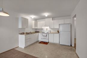 Grande Prairie apartment for rent - A spacious kitchen here at Carrington Place with white cabinets, light countertops, and a double-basin sink, featuring a white stove and refrigerator and an open layout with bright overhead lighting.