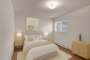 Grande Prairie apartment for rent - A cozy bedroom here at Carrington Place with soft carpet and neutral walls, featuring a neatly staged bed with light bedding, matching nightstands with lamps, and a large window with blinds for natural light.