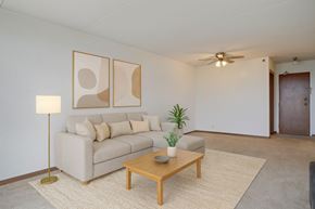 Regina apartment for rent - A bright living room here at Centre Pointe Plaza featuring a spacious light gray sectional with neutral throw pillows, a warm wood coffee table, and a soft area rug, complemented by simple wall art, a modern floor lamp, and fresh greenery for a cozy, welcoming feel.