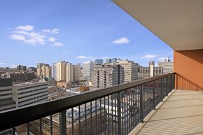 Regina apartment for rent - A sunny balcony here at Centre Pointe Plaza featuring a spacious outdoor layout with sturdy railing details, open-air cover for shade, and sweeping city skyline views under a bright blue sky for a refreshing, scenic escape.