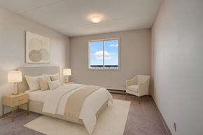 Regina apartment for rent - A bright bedroom here at Centre Pointe Plaza featuring a cozy bed with crisp white bedding, soft neutral accent pillows, and a warm beige throw, complemented by matching nightstands with modern lamps, simple wall art, and a comfy accent chair by the window for a calm, welcoming feel.