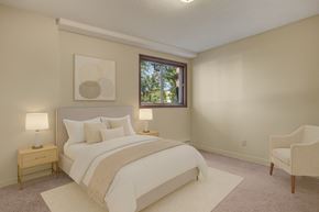 Saskatoon apartment for rent - A bright bedroom here at Edgemont Heights featuring a cozy bed with crisp white bedding and soft neutral pillows, paired with matching nightstands and warm table lamps, plus simple wall art and a plush accent chair for a calm, relaxing retreat.
