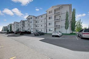 Leduc apartment for rent - A bright exterior view here at Edgewood Estates featuring a well-maintained apartment community with private balconies, a convenient parking area, and mature trees, all set against a clear blue sky for a welcoming first impression.