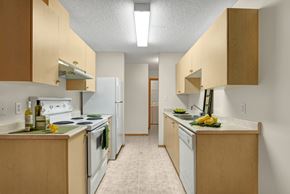 Leduc apartment for rent - A bright kitchen here at Edgewood Estates featuring warm light-wood cabinetry, spacious countertops, and a clean galley-style layout with full-size white appliances, plus simple green accents and everyday essentials for a fresh, functional space.