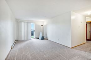 Leduc apartment for rent - A bright living room here at Edgewood Estates featuring soft neutral carpet, large sliding patio doors with vertical blinds for natural light, and an open layout with plenty of space to relax, plus a simple floor lamp and minimal decor for a clean, welcoming feel.
