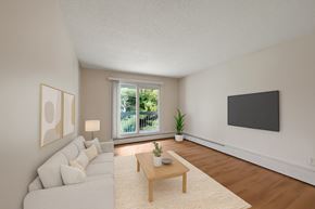 St. Albert apartment for rent - A bright living room here at Gateway Gardens featuring warm wood-style flooring, a cozy light sofa with neutral pillows, and a simple coffee table on a soft area rug, plus a sliding glass door with balcony views and calming greenery outside.
