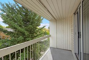 St. Albert apartment for rent - A private balcony here at Gateway Gardens featuring a covered outdoor space with railing views of mature trees and a quiet neighborhood setting, offering a peaceful spot to enjoy fresh air.