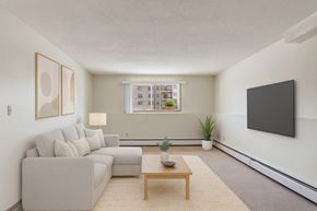 St. Albert apartment for rent - A bright living room here at Gateway Square featuring a cozy light-gray sectional with soft neutral pillows, paired with modern wall art, a warm wood coffee table on a plush area rug, and a few simple plants for a clean, relaxing feel.