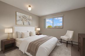St. Albert apartment for rent - A bright bedroom here at Gateway Square featuring a cozy bed with crisp white bedding and soft neutral pillows, paired with matching nightstands and warm table lamps, plus elegant wall art and a plush accent chair for a calm, relaxing retreat.