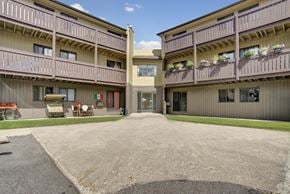 Saskatoon apartment for rent - A welcoming courtyard exterior here at Kingsmere with multi-level apartment buildings, private balconies, landscaped grass, and a central walkway leading to a secure building entrance under a bright blue sky.