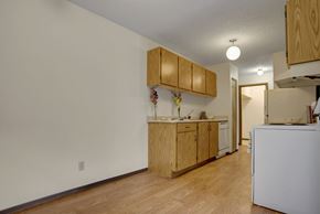 Saskatoon apartment for rent - A bright, open kitchen here at Kingsmere with light wood cabinets, neutral countertops, wood-style flooring, and white appliances, featuring ample counter space and overhead lighting for a clean, functional feel.