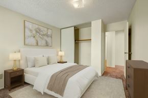 Edmonton apartment for rent - A calm, inviting bedroom here at Lakewood Heights with soft neutral walls, plush carpet, a comfortable bed with layered bedding, warm bedside lighting, and a sliding-door closet that adds convenient storage.
